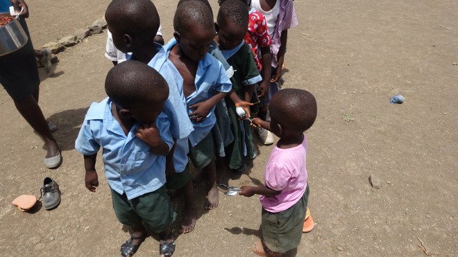 Little S.P. hands out spoons to the children lined up to get their lunch.